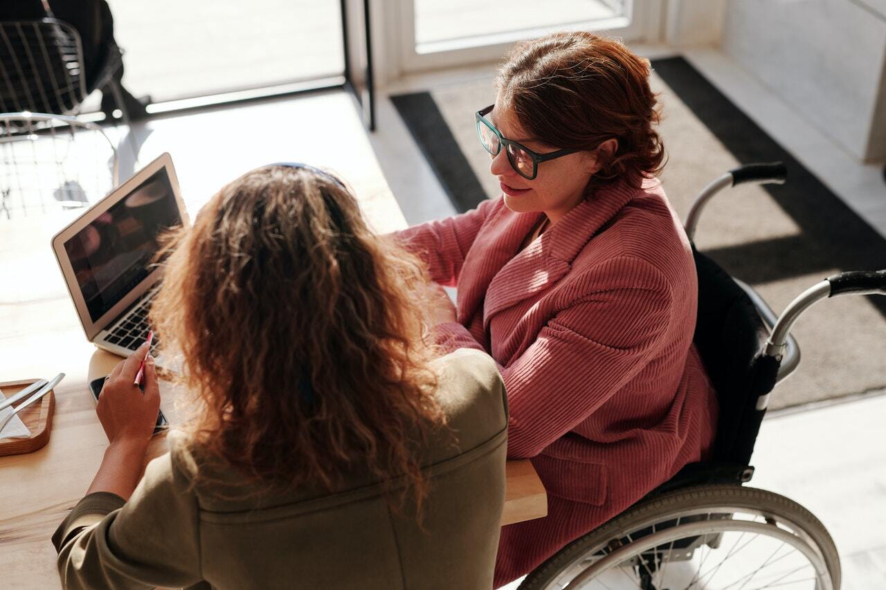 Women in wheelchair on computer speaking to woman about registered disability savings plan