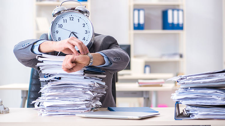 Man behind a large stack of tax files with a clock on top checking the time