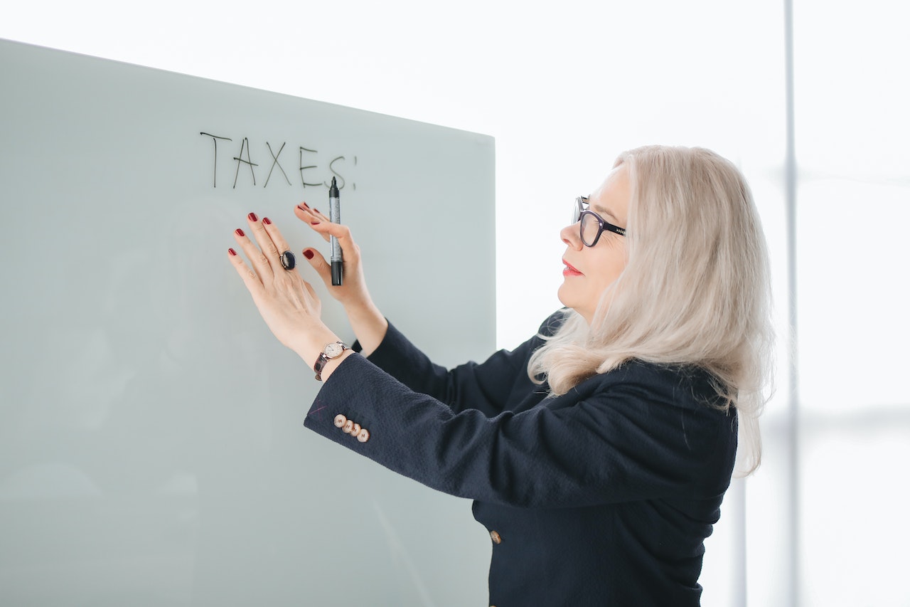 Women with gray hair in glasses pointing to word taxes on a white board