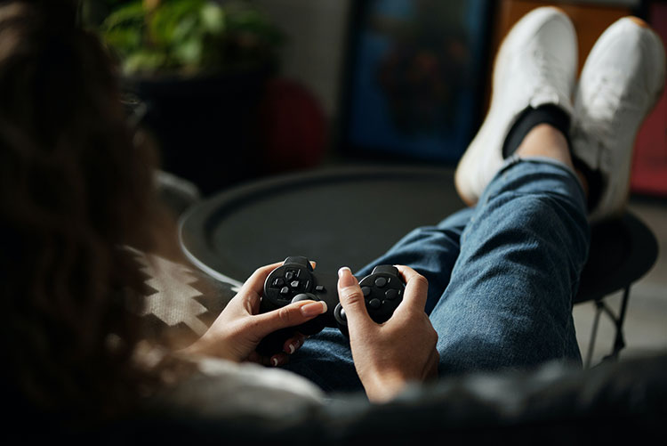 Person holding a video game controller and playing a video game with their feet up on a table
