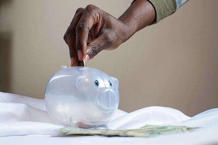 Person putting savings into clear piggy bank
