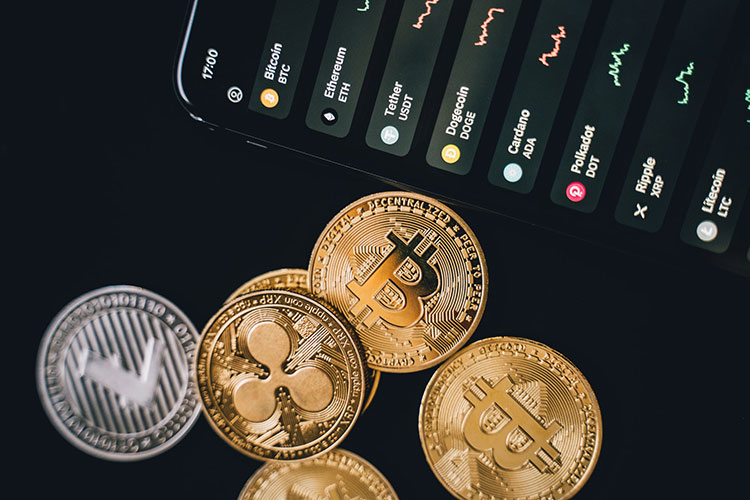 Image of different crypto coins beside phone showing crypto stocks