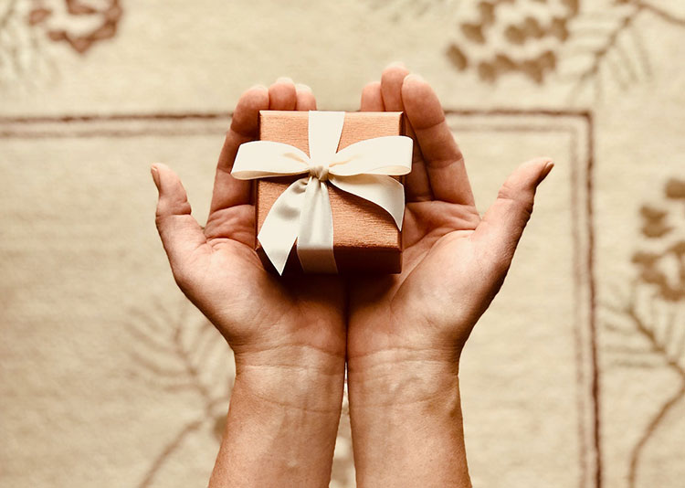 Picture of hands holding small brown gift box with white bow