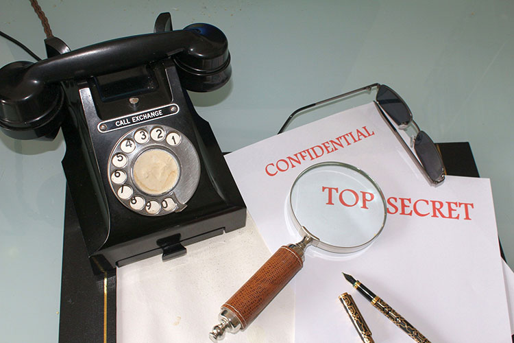 Picture of phone beside a stack of papers stating confidential top secret with a magnifying glass on top
