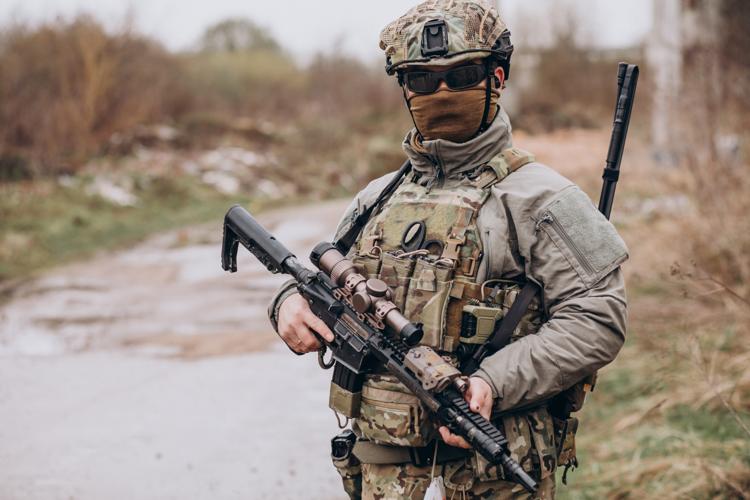 Armed forces member in camouflage and mask holding a rifle