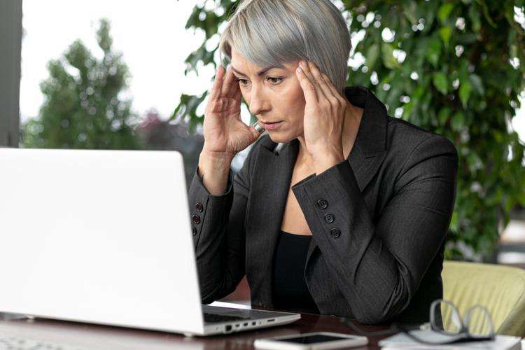 Businesswoman holding her head in confusion, looking at her laptop