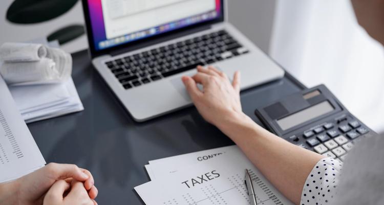 Woman using a calculator and laptop with tax forms on the desk