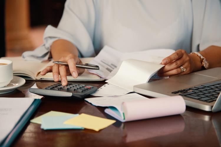 Closeup of a woman in a dress shirt at a desk with paperwork using a calculator and a pen