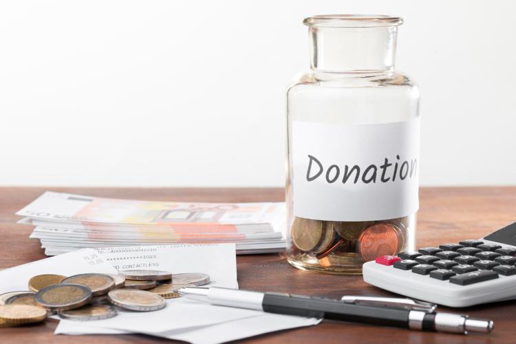 A jar of change labelled Donations on a table with other coins and bills, a pen, and a calculator.