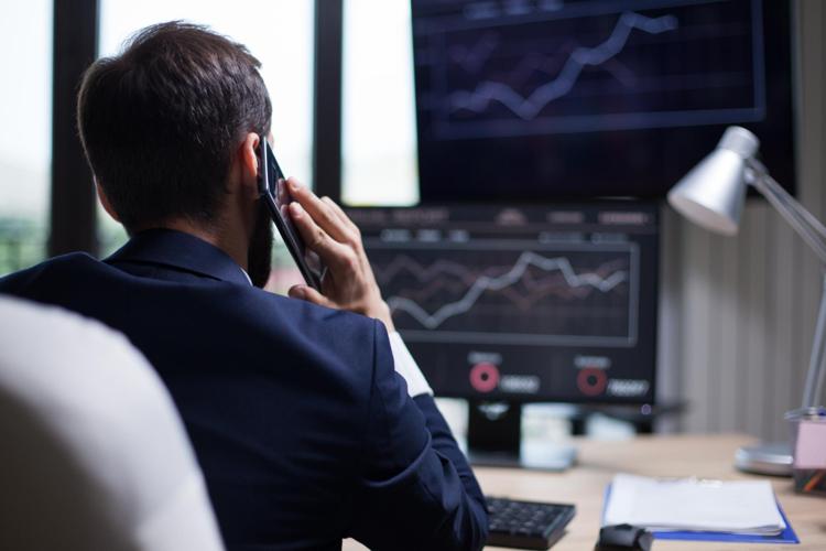 Back view of A young businessman on a phone call in front of a screen displaying financial information.