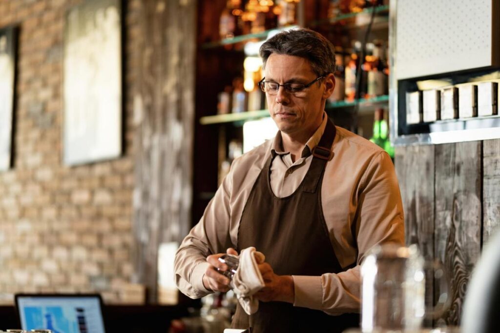 Bartender wearing an apron cleaning a shot glass.