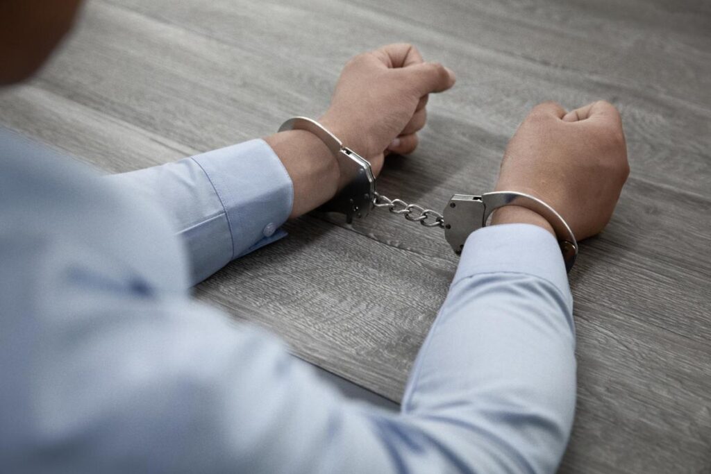 Closeup shot of male hands in handcuffs on a wooden table.
